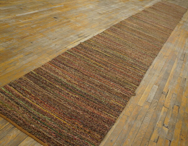 Textured, multicolored brown runner rug with thin bright stripes rests upon a worn hardwood floor.