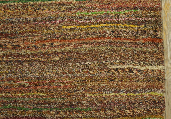 Shaggy multicolor rug texture displays brown flecks mixed with vivid horizontal stripes on a wood floor.