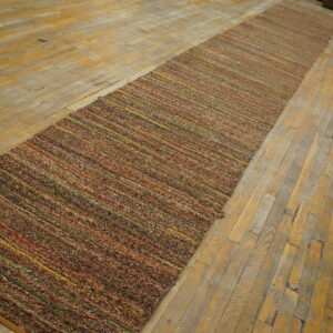 Textured brown runner rug featuring thin colorful stripes sits on a distressed wood floor.