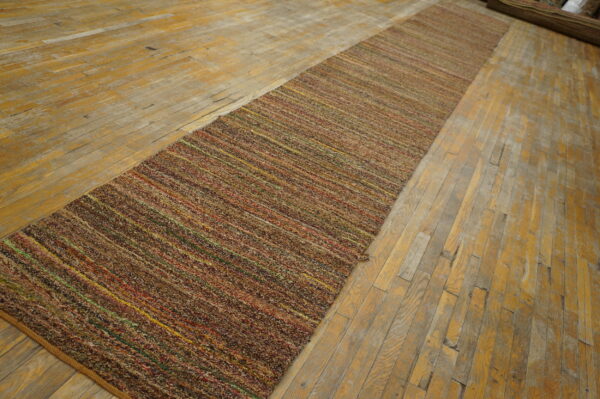 Textured brown runner rug featuring thin colorful stripes sits on a distressed wood floor.