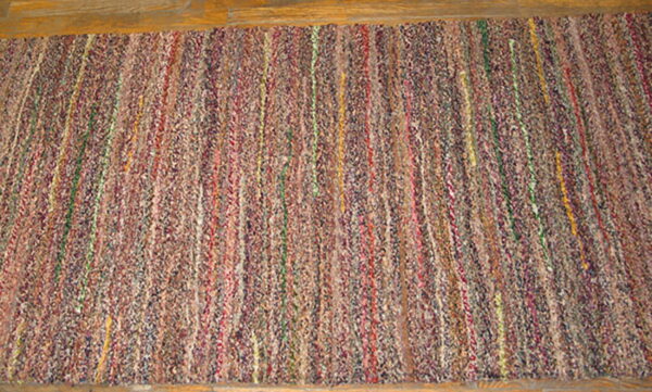 Textured runner rug with multicolored vertical braided segments lying on light wood planks.