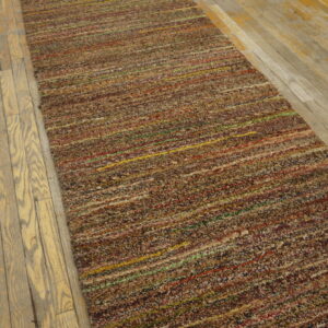 Textured multicolored runner rug with horizontal stripes rests on worn light hardwood flooring.