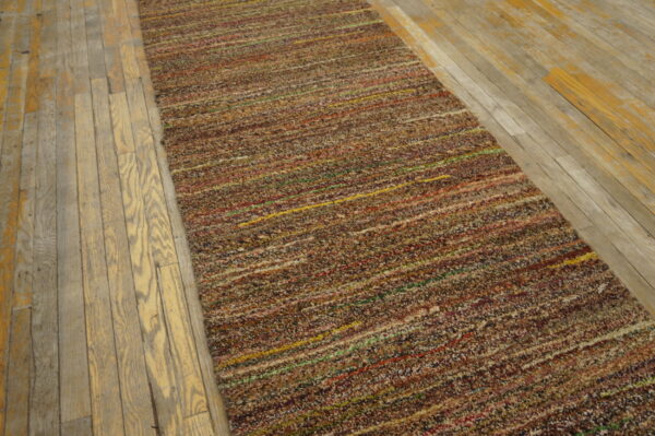 Textured multicolored runner rug with horizontal stripes rests on worn light hardwood flooring.