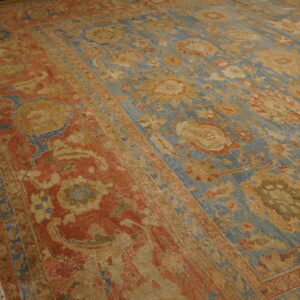 Close-up view of a large floral rug in blue, rust, and gold on worn hardwood flooring.