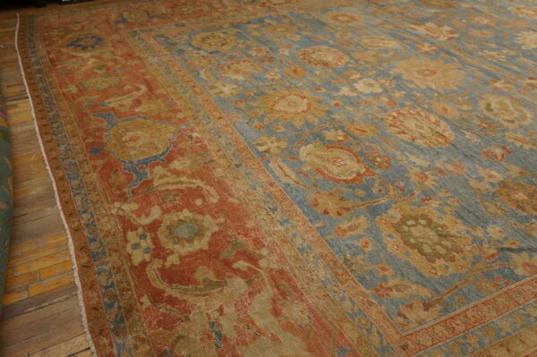Close-up view of a large floral rug in blue, rust, and gold on worn hardwood flooring.