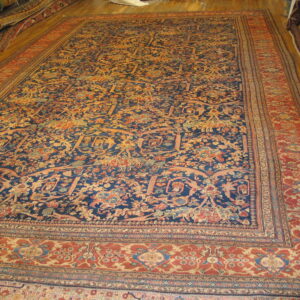 Ornate navy blue rug with dense floral pattern and wide rust border on a hardwood floor.