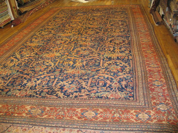 Ornate navy blue rug with dense floral pattern and wide rust border on a hardwood floor.