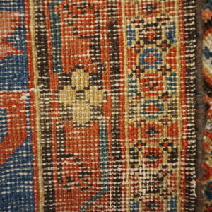 Close-up of two adjoining rugs displaying geometric flatweave patterns in rust, blue, black, and tan.