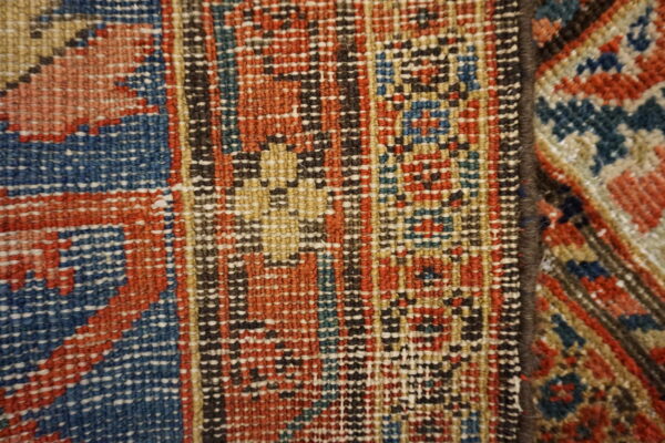 Close-up of two adjoining rugs displaying geometric flatweave patterns in rust, blue, black, and tan.