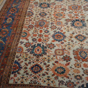 Floral pattern rug in indigo, rust, and cream colors, with a distressed border on wood plank flooring.