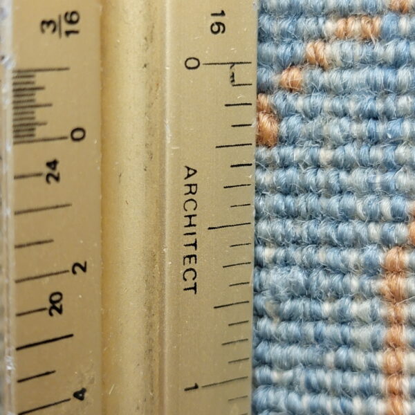 Close-up of blue, white, and tan rug pile texture next to an architect scale ruler.