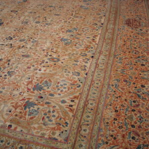 Muted cream and orange rug with a detailed botanical and bird pattern lies on wooden flooring.