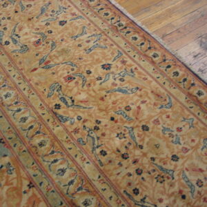Gold rug featuring repeated blue stylized animal figures and thin red borders rests on rustic wood flooring.
