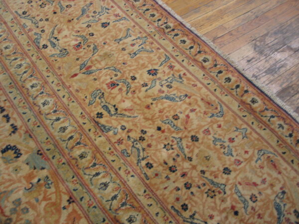 Gold rug featuring repeated blue stylized animal figures and thin red borders rests on rustic wood flooring.