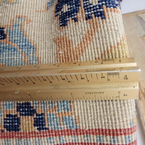 Detailed view of looped rug texture in navy, light blue, cream, and rust with a ruler.