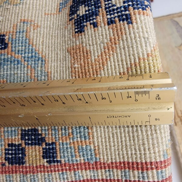 Detailed view of looped rug texture in navy, light blue, cream, and rust with a ruler.