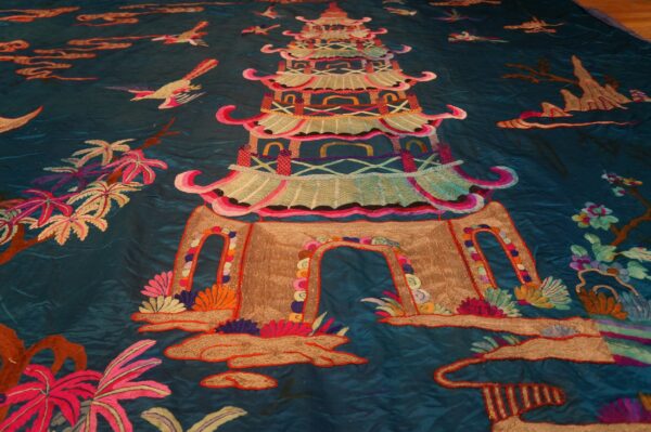 Deep teal embroidered textile featuring a vibrant, multicolored central pagoda surrounded by birds and foliage.