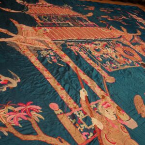 Teal textile with elaborate red, pink, and gold figures, a pagoda, and trees depicted across the surface.