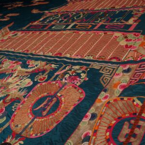 Detailed view of a dark teal textile with elaborate embroidered dragons and medallions in bright, contrasting colors.