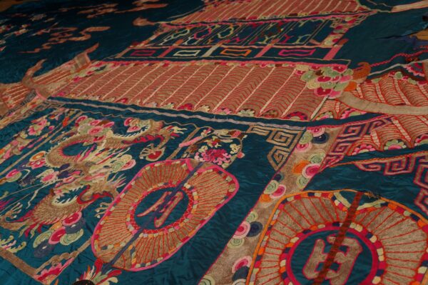 Detailed view of a dark teal textile with elaborate embroidered dragons and medallions in bright, contrasting colors.