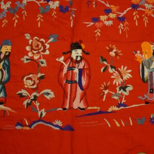 Detailed multicolored embroidery of three figures and flowers on a vibrant red, flat-pile surface.