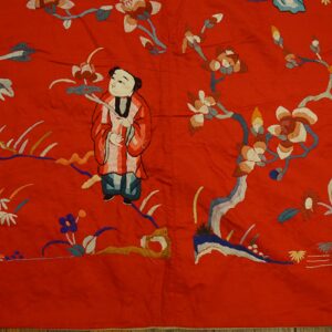 Scarlet flatweave textile embroidered with a central figure, multicolored flowers, and foliage on a wood floor.