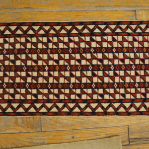 Cream and dark red geometric runner rug with low pile lies on distressed light brown wood flooring.