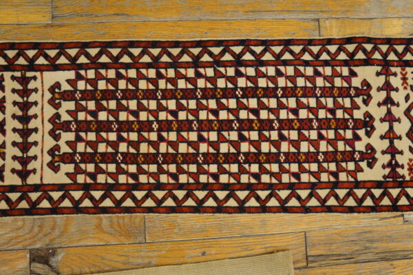 Cream and dark red geometric runner rug with low pile lies on distressed light brown wood flooring.