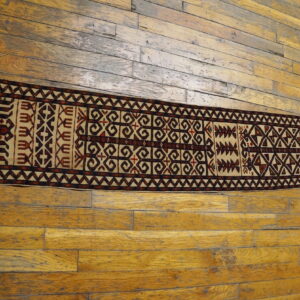 Narrow runner rug features dark brown and beige geometric motifs centered on distressed plank flooring.