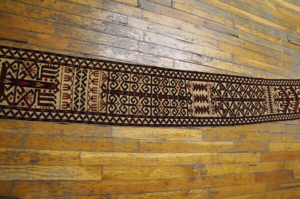 Narrow runner rug features dark brown and beige geometric motifs centered on distressed plank flooring.