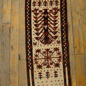 Narrow cream runner rug with deep red and blue tribal patterns resting on distressed wood flooring.