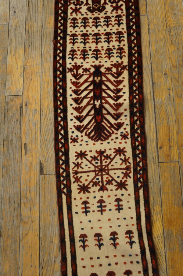 Narrow cream runner rug with deep red and blue tribal patterns resting on distressed wood flooring.