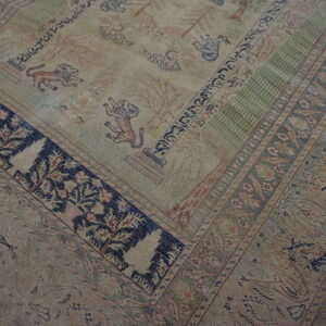 Muted beige rug featuring a patterned field with lions and trees, framed by complex dark blue borders.