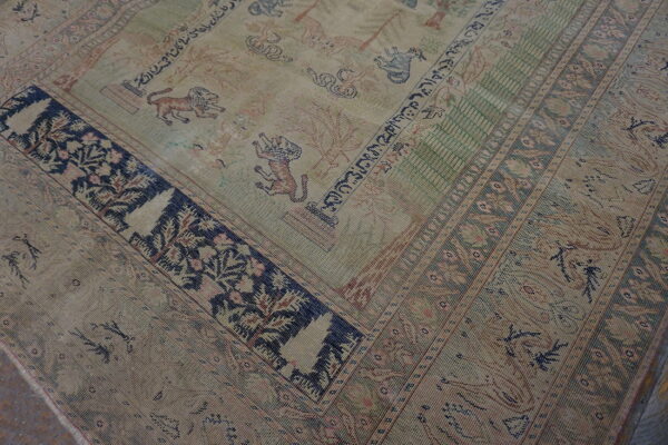 Muted beige rug featuring a patterned field with lions and trees, framed by complex dark blue borders.