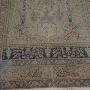 Low-pile beige and tan rug with faded bird, urn, and botanical motifs in green, pink, and navy.