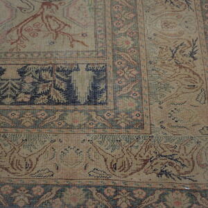 Detailed view of a beige rug with faded navy and pink traditional borders on gray plank flooring.