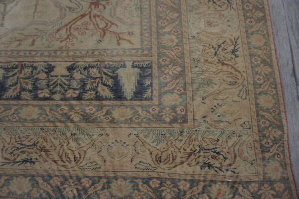 Detailed view of a beige rug with faded navy and pink traditional borders on gray plank flooring.
