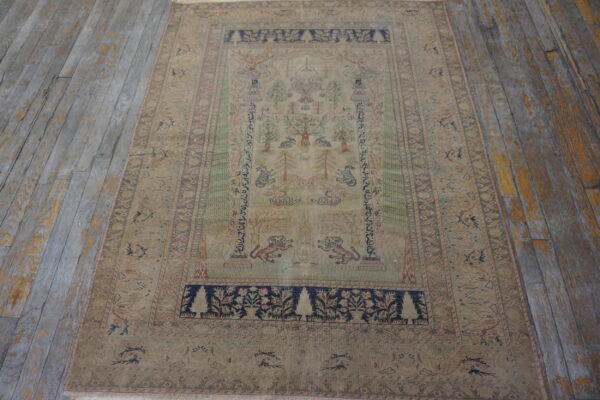 Muted pictorial rug featuring fauna and flora, with navy accents, placed on distressed gray wood flooring.