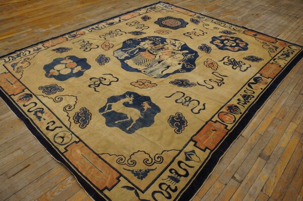 Tan square rug featuring blue medallions, rust accents, cloud patterns, and a central figurative design on worn wood floors.