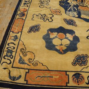 Close-up of a golden yellow rug patterned with navy blue clouds and orange traditional figures on worn hardwood.