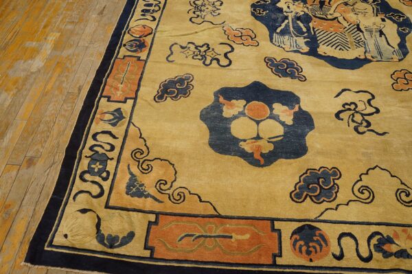 Close-up of a golden yellow rug patterned with navy blue clouds and orange traditional figures on worn hardwood.