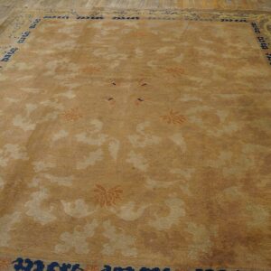 Muted gold rug with tone-on-tone pattern, rust flowers, and a navy border on wide wood planks.