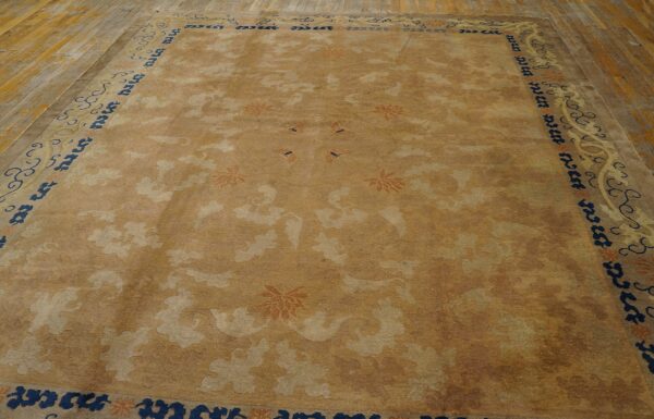 Muted gold rug with tone-on-tone pattern, rust flowers, and a navy border on wide wood planks.