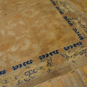 Golden tan rug with subtle floral designs features a wide border outlined in dark blue on rough plank flooring.