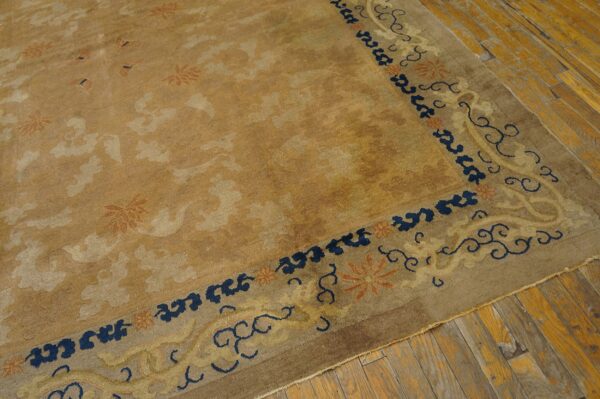 Golden tan rug with subtle floral designs features a wide border outlined in dark blue on rough plank flooring.