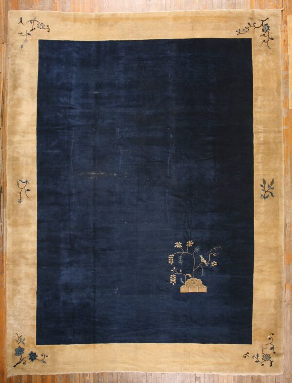 Navy and tan border rug with a stylized tree motif and a small bird, displayed on wood plank flooring.
