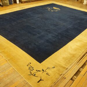 A large navy blue rug with a wide golden yellow border featuring corner floral motifs lies on distressed wood flooring.