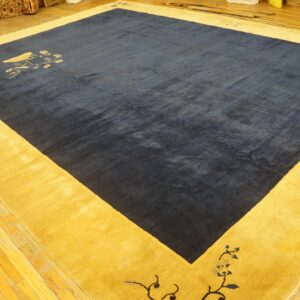 Navy blue rug with a wide gold border and stylized floral patterns on light wood floors.