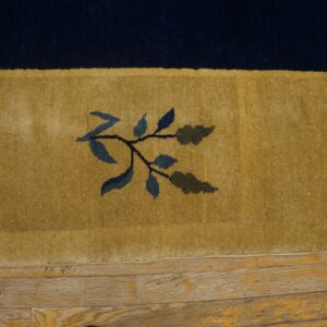Navy and gold rug border with a blue leaf motif rests on worn wooden planks.