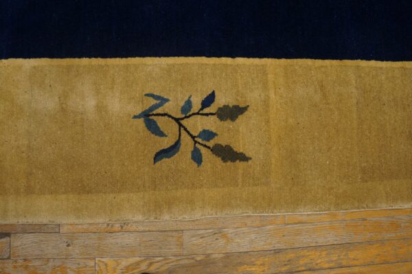 Navy and gold rug border with a blue leaf motif rests on worn wooden planks.